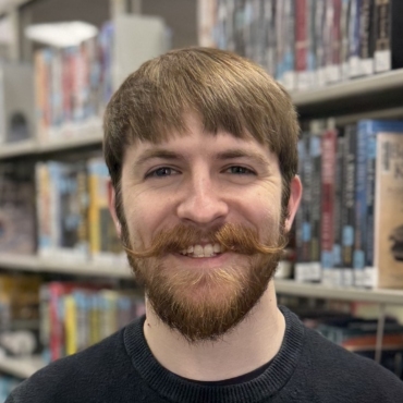 Headshot of Kasen Urhammer, Marketing & PR Manager, smiling in front of bookshelves.